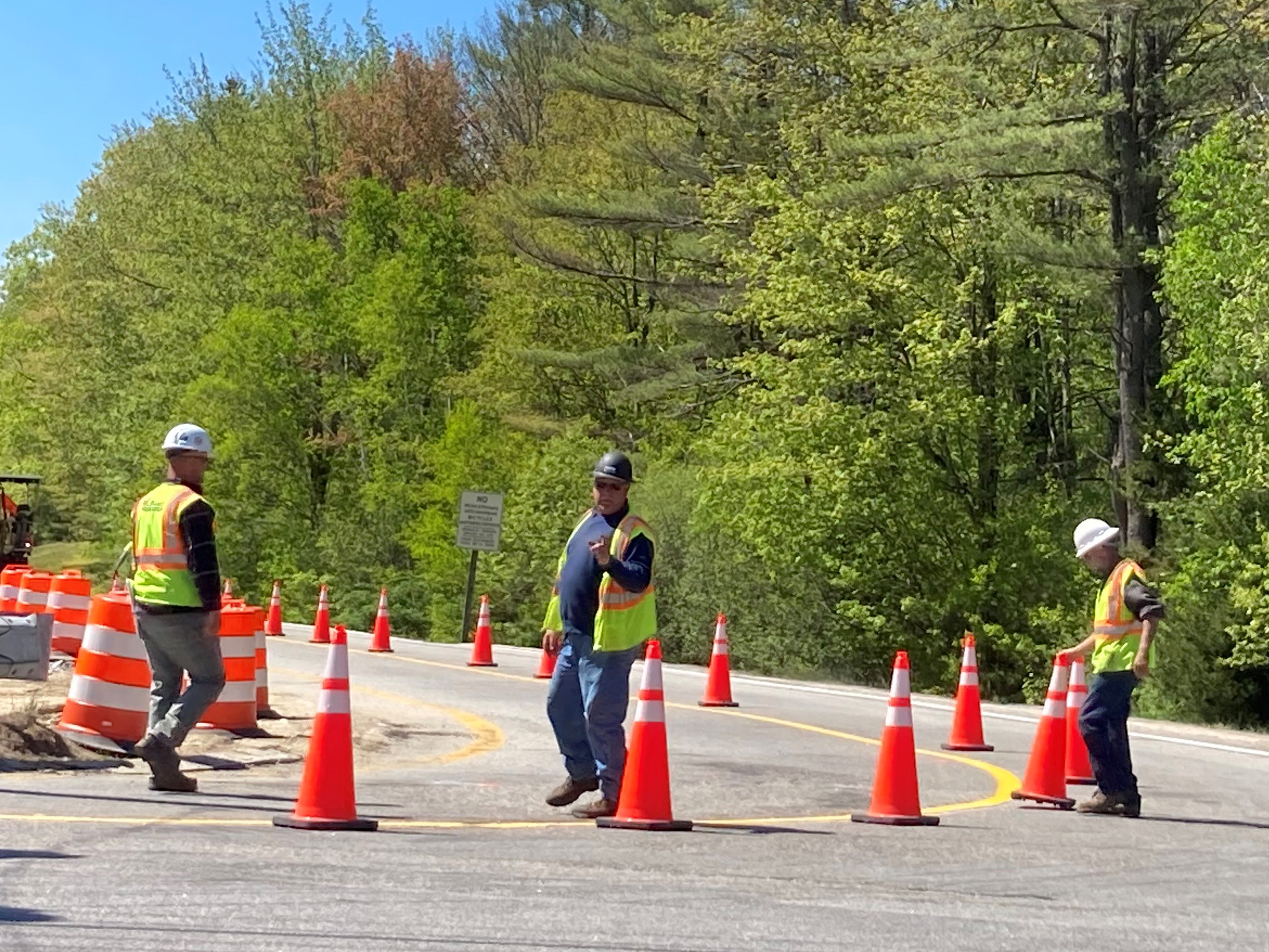 Workers place large safety cones in the road to indicate temporary lanes.